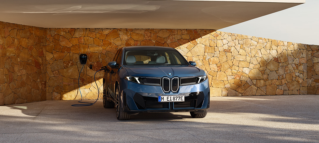 Das Bild zeigt in der Mitte einen dunkelblauen BMW iX3, ein großes, sportliches Elektro-SUV. Er steht im Freien vor einer Ladestation mit Blick aufs Meer. Die Vorderseite ist markant mit beleuchteten Elementen, die an die typische BMW-Niere erinnern. Auf der rechten Seite sind zwei kleinere Bilder: oben sieht man das futuristische, fahrerorientierte Cockpit mit einem großen, breiten Display, auf dem Informationen wie Navigation und Unterhaltung angezeigt werden. Das Lenkrad ist nicht rund, sondern eher eckig geformt. Unten sieht man die Rückansicht des Autos, die durch schmale, horizontale Rückleuchten und eine tiefe, aerodynamische Form gekennzeichnet ist.