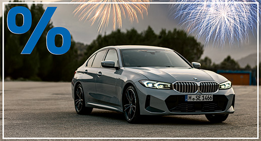 Diese Werbegrafik zeigt eine elegante BMW 318i Limousine in einem modernen Grauton, die auf einer freien Asphaltfläche parkt. Das Fahrzeug ist leicht schräg von vorne abgelichtet, was die sportliche Frontpartie und die flache Silhouette betont. Im Hintergrund ist eine sanfte, bewaldete Hügellandschaft unter einem bewölkten Dämmerungshimmel zu erkennen.  Der Himmel wird durch zwei große, leuchtende Feuerwerke in Gold und hellem Blau feierlich erhellt. Wie bei der gesamten Aktionsserie befindet sich in der oberen linken Ecke das markante, große blaue Prozentzeichen, und das gesamte Motiv wird von einem schmalen weißen Rahmen umschlossen.