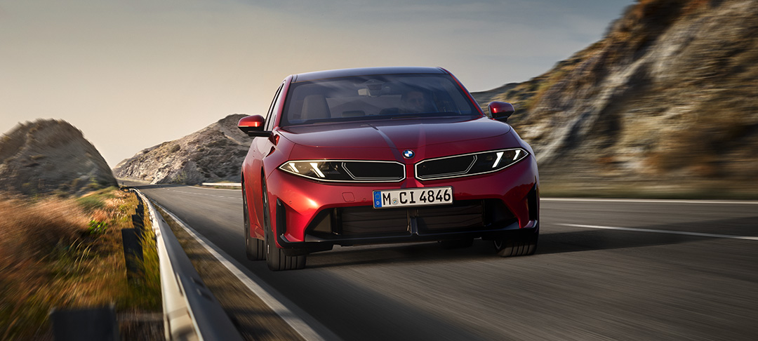 Neue rote BMW 3er Limousine in dynamischer Frontansicht auf einer kurvenreichen Bergstraße. Die markante BMW Niere, schmalen LED-Scheinwerfer und sportlichen Lufteinlässe prägen das Design.