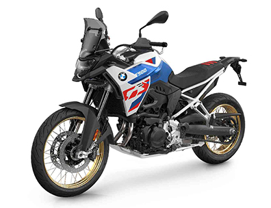  Auf dem Bild ist eine BMW F 900 GS abgebildet, ein großes, weiß-blau-rotes Motorrad, das auf einem weißen Hintergrund steht.  Das Motorrad ist in einem hellen, sonnigen Licht und steht seitlich zur Kamera. Es hat goldene Speichenräder, eine Verkleidung im BMW-Motorsportdesign in den Farben Weiß, Blau und Rot. Es ist sauber und glänzt, als wäre es brandneu.