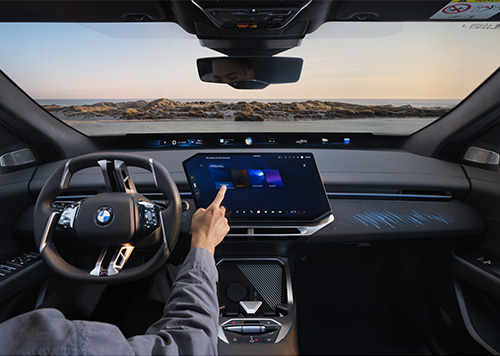 Moderner Innenraum des BMW iX4 mit großem Touchdisplay, digitaler Instrumentenanzeige und einer Person, die den Bildschirm bedient.