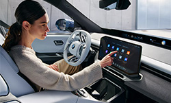 Frau bedient das zentrale Touchdisplay im modernen Innenraum eines BMW Neue Klasse Fahrzeugs