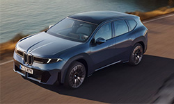 Blauer BMW iX3 der Neuen Klasse aus erhöhter Front- und Seitenperspektive auf einer Straße