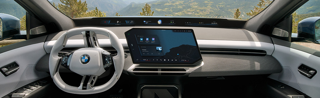 Moderner BMW Neue Klasse Innenraum mit weißem Lenkrad, großem Touchdisplay und digitaler Instrumentenanzeige vor einer Berglandschaft.