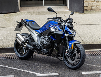 Blaue BMW R 1300 R in sportlicher Front-Seitenansicht auf einem Parkplatz.