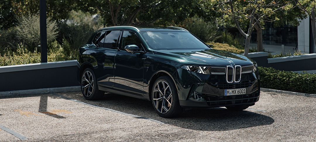 Dunkelgrüner BMW X5 40 xDrive in sportlicher Front- und Seitenansicht mit markanter BMW Niere und großen Leichtmetallrädern vor grüner Kulisse.