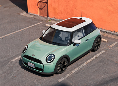 Mintgrüner Mini Cooper im Seitenprofil vor grünem Gebäude.