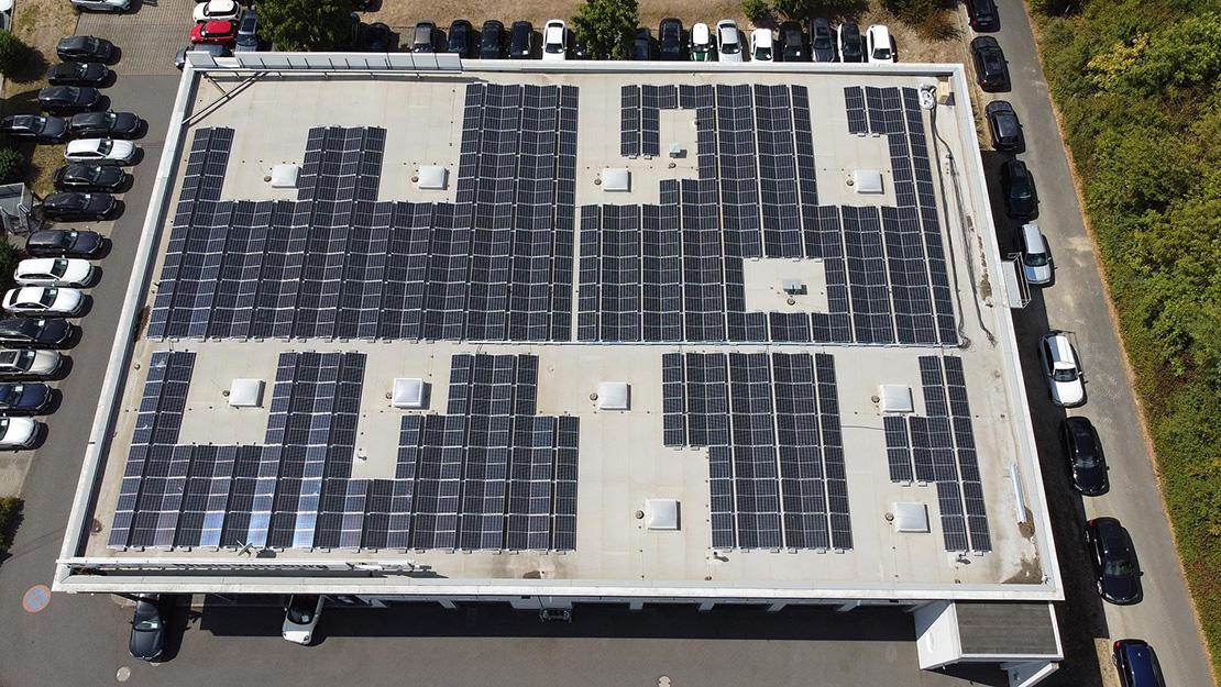 Photovoltaik-Anlage BMW Autohaus Rhein Dach eines großen Gebäudes mit Solarmodulen, umgeben von geparkten Autos.