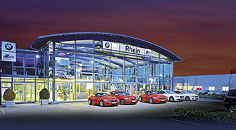 BMW Rhein Standort Ludwigsburg Modernes BMW Rhein Autohaus bei Dämmerung mit beleuchteten Schaufenstern und geparkten BMWs