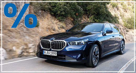 Dunkelblaue BMW 520i Limousine in Fahrt auf einer Bergstraße; blaues Prozent-Symbol oben links.