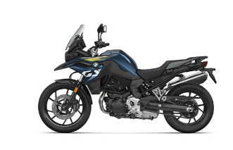  Ein Motorrad im Adventure-Stil von BMW, das in einem dunklen Blauton gehalten ist. Es steht schräg von der Seite vor einem weißen Hintergrund. Es hat gelbe Streifen auf der Verkleidung und ist mit einer Windschutzscheibe, einem Vorderradschutzblech und einem Gepäckträger am Heck ausgestattet.