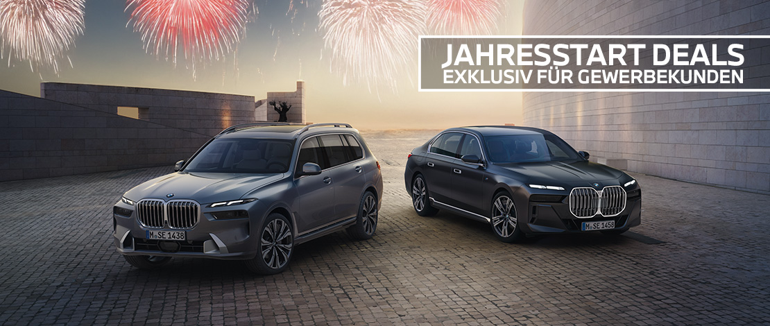 Dieses breitformatige Werbebanner gleicht dem vorherigen Motiv fast exakt und zeigt einen imposanten, hellgrauen BMW X7 sowie eine elegante, dunkelgraue BMW 7er Limousine. Die beiden Fahrzeuge stehen auf einem weitläufigen Pflastersteinplatz vor einer modernen, hellen Architekturkulisse, während im Hintergrund ein goldener Sonnenuntergang über dem Meer zu erahnen ist. Der obere Bildrand wird von festlichen, hell leuchtenden Feuerwerken in Weiß- und Rottönen geschmückt. Der einzige Unterschied liegt im Textfeld oben rechts, welches hier in fetten weißen Buchstaben die Aufschrift „JAHRESSTART DEALS EXKLUSIV FÜR GEWERBEKUNDEN“ trägt.