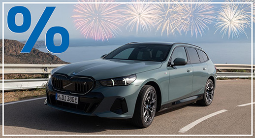 Diese Werbegrafik zeigt einen modernen BMW i5 Touring in einem eleganten Salbeigrün, der auf einer Küstenstraße parkt. Das vollelektrische Kombi-Modell ist schräg von vorne abgelichtet, wodurch die sportliche Front mit den dunklen Akzenten und die fließende Silhouette des Hecks betont werden. Im Hintergrund erstreckt sich eine ruhige Meeresbucht unter einem hellen Dämmerungshimmel, flankiert von kargen Küstenfelsen.  Der obere Bildrand wird von einer Reihe goldener und weißer Feuerwerksexplosionen geschmückt, die über dem Horizont erstrahlen. Das für die Aktionsserie typische große blaue Prozentzeichen oben links sowie der schmale weiße Rahmen runden das Design ab.