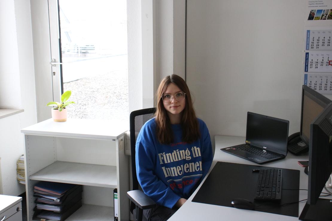 Eine junge Frau sitzt konzentriert an ihrem Schreibtisch mit zwei Monitoren im Büro.