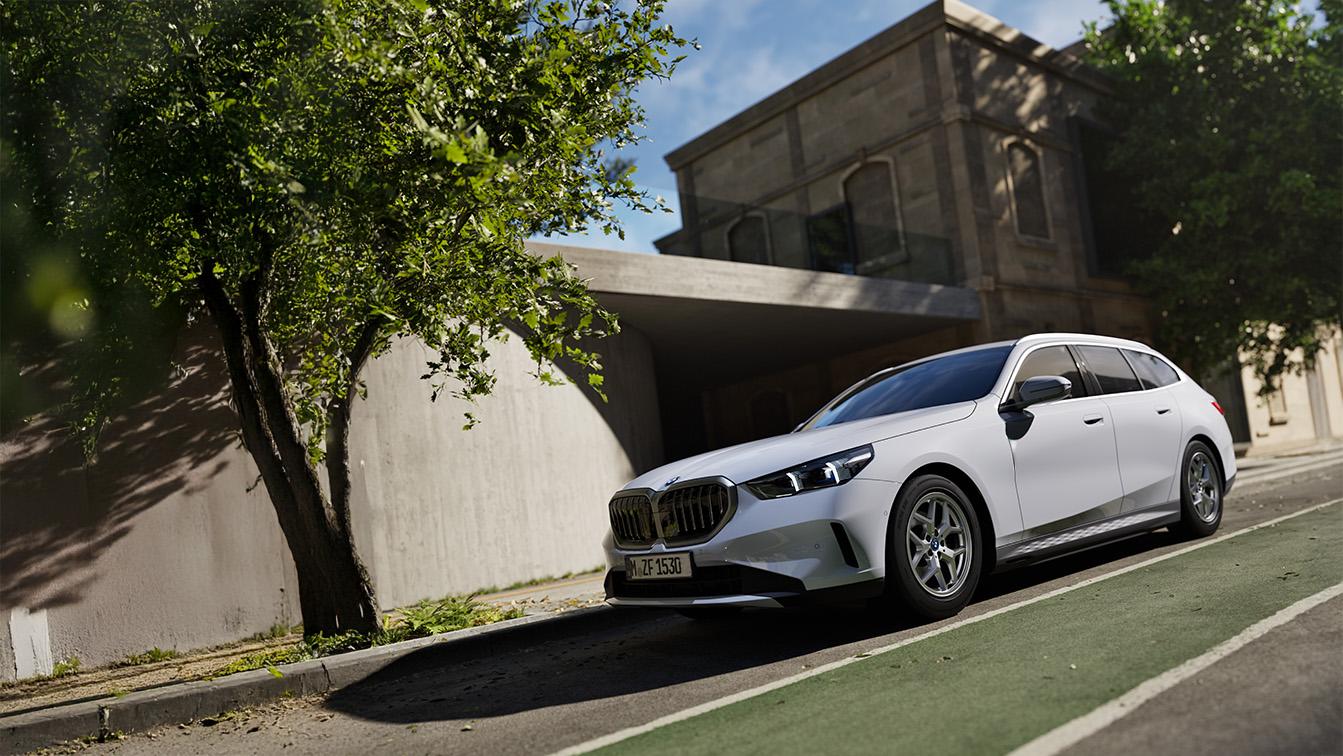 Weißer BMW 5er Touring in Front-Seitenansicht, geparkt an einer Straße vor einem modernen Gebäude.