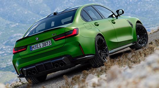 Heckansicht einer leuchtend grünen BMW M3 Competition Limousine, die auf einer schrägen, felsigen Straße steht.