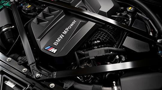 Nahaufnahme eines BMW M Power Motors mit schwarzer Abdeckung und dem BMW M Logo. Man sieht die Querstrebe zur Stabilisierung des Motors und verschiedene technische Komponenten im Motorraum.