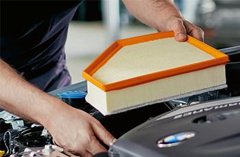 BMW Servicetechniker setzt einen Luftfilter in den Motorraum eines Fahrzeugs ein.