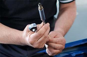 BMW Servicetechniker hält eine Zündkerze und ein Werkzeug in den Händen.