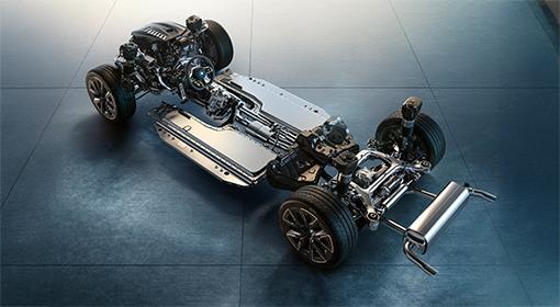 Das Bild zeigt das Fahrgestell eines Autos von schräg oben. Die Karosserie fehlt, sodass die mechanischen und elektrischen Bauteile sichtbar sind. In der Mitte ist die flache Batterie des Plug-in-Hybrids zu erkennen, während an der Vorder- und Rückseite die Aufhängungen, Räder, Bremsen und der Auspuff sichtbar sind.