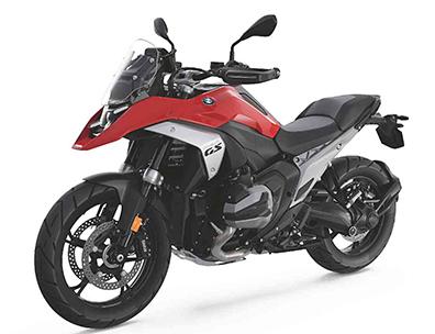  Auf dem Bild ist eine BMW R 1300 GS abgebildet, ein großes, rotes und schwarzes Motorrad, das auf einem weißen Hintergrund steht.  Das Motorrad ist in einem hellen, sonnigen Licht und steht seitlich zur Kamera. Es ist sauber und glänzt, als wäre es brandneu.