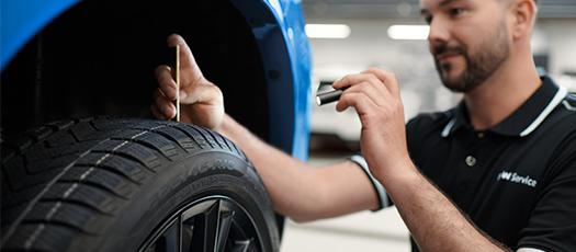 BMW Servicetechniker misst die Profiltiefe eines Reifens an einem blauen BMW.