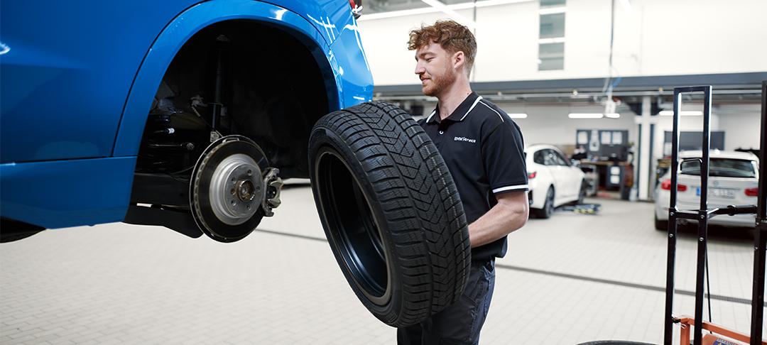 BMW Servicetechniker trägt ein Rad zu einem blauen BMW auf der Hebebühne