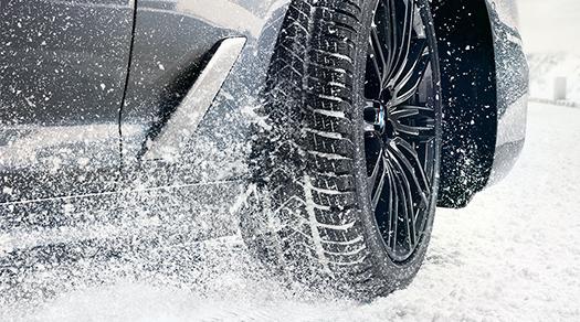 Nahaufnahme eines BMW Winterreifens bei der Fahrt durch Schnee.