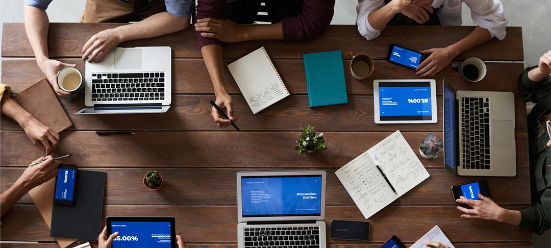 Eine Gruppe von Personen arbeitet gemeinsam an einem großen Tisch mit Laptops und Tablets.