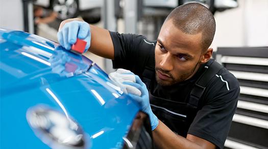 BMW Servicetechniker poliert die Oberfläche eines blauen BMW.