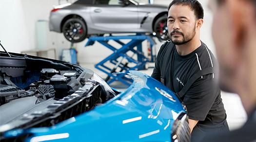 BMW Servicetechniker arbeitet an der Front eines blauen BMW in einer Werkstatt.