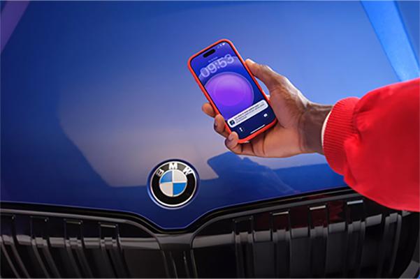 Hand hält ein Smartphone mit einer Service-Benachrichtigung vor der Front eines blauen BMW.