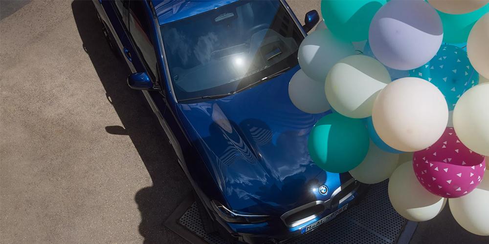 Blauer BMW aus der Vogelperspektive, teilweise umgeben von großen bunten Ballons.