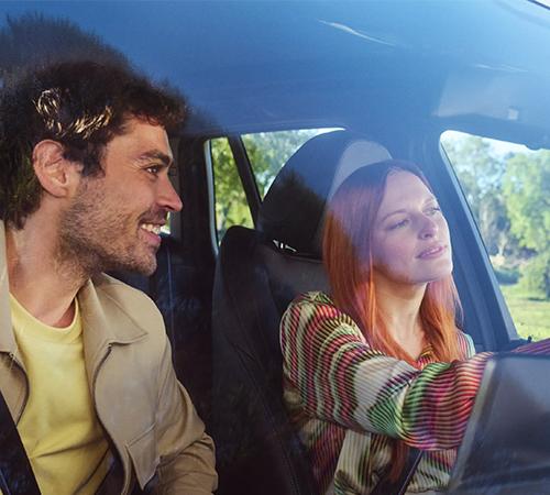 Frau sitzt am Steuer eines BMW, während ein Mann auf dem Beifahrersitz lächelnd zu ihr schaut.