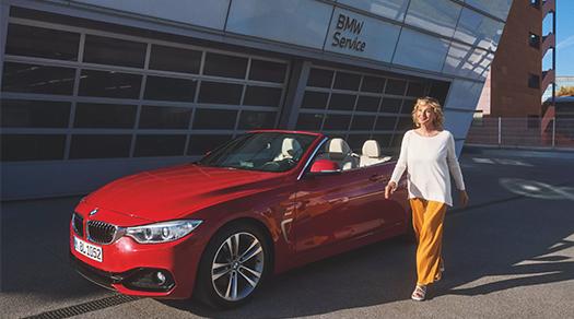 Frau steht neben einem roten BMW Cabrio vor einem BMW Service Gebäude.