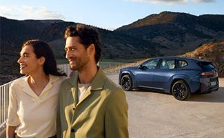 Paar vor einer Berglandschaft mit einem blauen BMW im Hintergrund.
