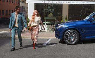 Paar geht Hand in Hand an einem blauen BMW vorbei.