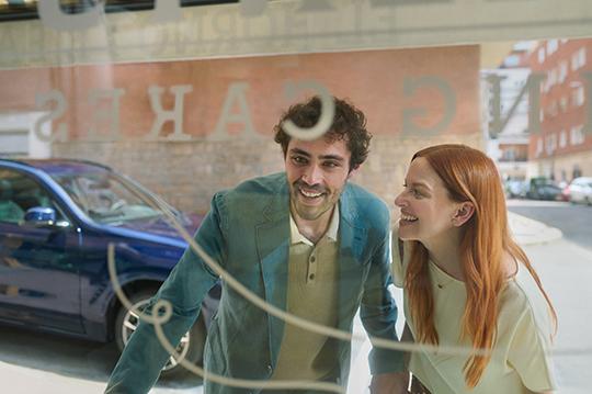 Lächelndes Paar schaut durch ein Schaufenster, während im Hintergrund ein blauer BMW steht.
