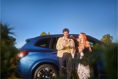 „Mann und Frau stehen neben einem blauen BMW und schauen gemeinsam auf ein Smartphone.“