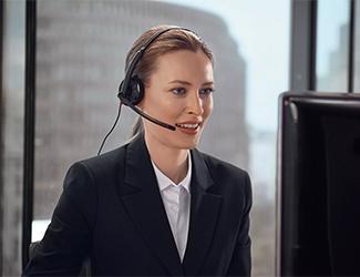 Mitarbeiterin mit Headset sitzt vor einem Bildschirm und unterstützt telefonisch bei einer Panne.