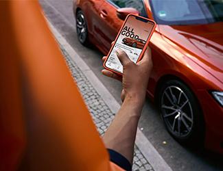 Person nutzt ein Smartphone neben einem geparkten roten BMW.