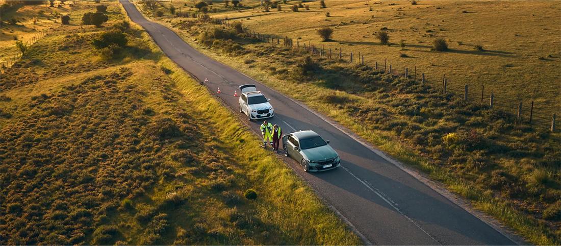 Luftaufnahme einer Pannensituation auf einer Landstraße mit zwei Fahrzeugen und zwei Personen in Warnwesten.