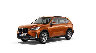Das Bild zeigt einen orangefarbenen BMW iX1, ein kompaktes SUV. Das Auto steht schräg von vorne auf einem weißen, leeren Hintergrund. Das Kennzeichen "M JE 1438" ist auf der vorderen Stoßstange zu sehen.