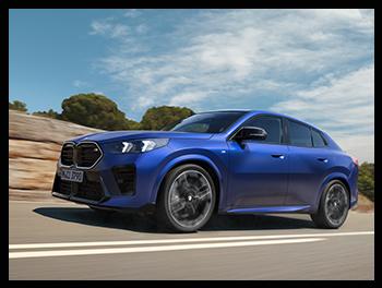 Ein blauer BMW X2 M35i in Fahrt auf einer Landstraße vor Felsen; die mattblaue Lackierung, die schwarze Doppelniere und die dynamische Coupe-Silhouette sind gut zu erkennen.