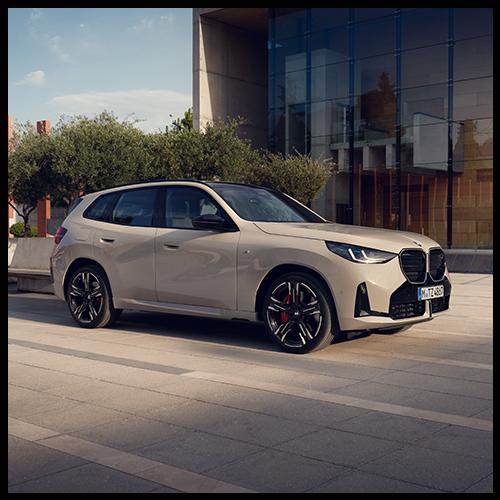 Diese Profilaufnahme des BMW X3 M50 vor moderner Architektur betont die gestreckte Linienführung, die großen M-Leichtmetallräder mit roten Bremssätteln und die bündigen Türgriffe.