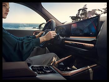 Im Innenraum des BMW X3 M50 sieht man das großflächige BMW Curved Display und die neue „Interaction Bar“ mit Kupfer-Akzenten, während eine Fahrerin das M-Lederlenkrad hält.