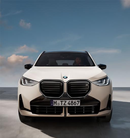 Das Foto zeigt die direkte Frontansicht eines BMW X3 M50 xDrive in einer hellen, fast beigefarbenen Lackierung (möglicherweise Alpinweiß oder ähnliches).  Das kompakte SUV steht auf einer flachen, grauen Oberfläche unter einem hellblauen Himmel mit einigen weißen Wolken. Der Wagen ist symmetrisch und frontal aufgenommen. Man sieht die große BMW-Doppelniere und schmale, moderne Scheinwerfer. Ein auffälliges Merkmal ist der kontrastierende, dunkle Bereich unterhalb des Kühlergrills, der dem Auto einen sportlichen Look verleiht.  Das Nummernschild lautet 'M TZ 4867'. Im Inneren, hinter der Windschutzscheibe, ist schemenhaft eine Person zu erkennen.