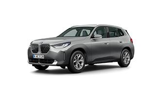Das Bild zeigt ein silbergraues, kastenförmiges SUV, den BMW iX3. Es steht schräg von vorne auf einem weißen, leeren Hintergrund. Das Kennzeichen "M NE 8261" ist auf der vorderen Stoßstange zu sehen.