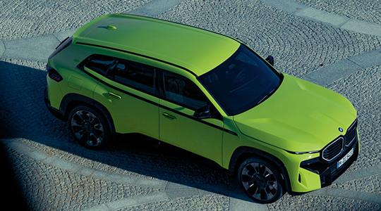 Ein leuchtend lindgrüner BMW XM SUV mit schwarzen Akzenten, von schräg oben gesehen, parkt auf einer gepflasterten Fläche.
