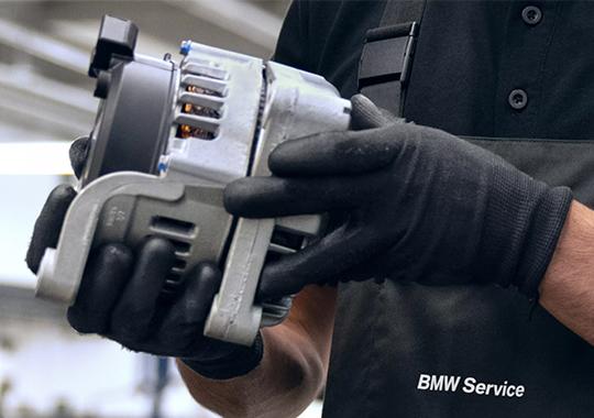 BMW Servicetechniker hält ein wiederaufbereitetes Fahrzeugbauteil in den Händen.